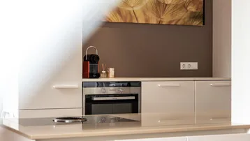 Moderne Küchenzeile mit integriertem Backofen, Induktionskochfeld und Kaffeemaschine.