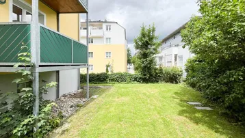 Gebäudeansicht mit Rasenfläche und Balkonen, umgeben von Bäumen und Sträuchern.