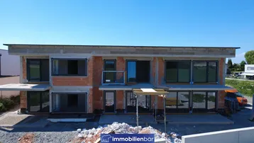 Modernes zweistöckiges Gebäude im Rohbau mit großen Fenstern und Flachdach unter blauem Himmel.