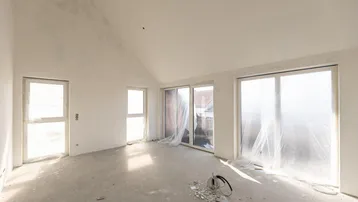 Heller, unfertiger Wohnraum mit großen Fenstern und schrägen Decken, bereit für den Ausbau.