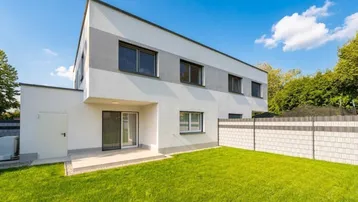 Moderne Doppelhaushälfte mit gepflegtem Rasen und kleiner Terrasse im Gartenbereich.
