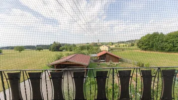 Blick vom Balkon über eine weite grüne Landschaft mit Feldern und Bäumen.