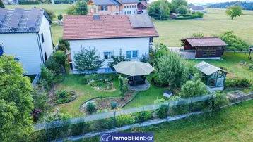Luftaufnahme des Einfamilienhauses mit gepflegtem Garten, Sitzbereich und Gewächshaus in ländlicher Umgebung.