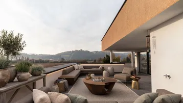 Geräumige Terrasse mit moderner Lounge-Möblierung, Feuerstelle und weitem Blick ins Grüne.