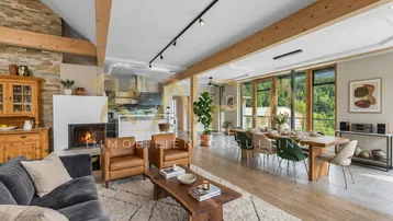 Offener Wohn-Essbereich mit Kamin, Holzbalken und moderner Küche im Hintergrund.