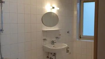 Helles Badezimmer mit weißen Fliesen, Badewanne und Fenster für natürliches Tageslicht.