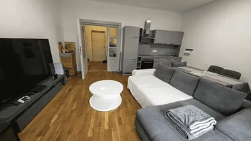 Geräumiger Wohnbereich mit Holzboden, großem Sofa und integrierter Küchenzeile in modernem Stil.