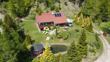 Luftaufnahme des Anwesens mit Haupthaus, Nebengebäude, Teich und umgebendem Wald.