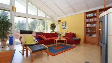 Gemütliches Wohnzimmer mit rotem Sofa, Holzboden und Blick auf die Natur durch große Fenster.