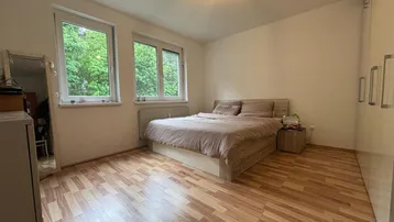 Helles Schlafzimmer mit Laminatboden, großem Fenster und Blick ins Grüne.
