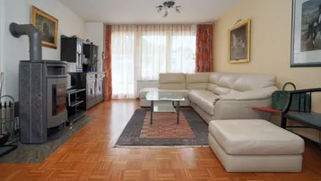 Gemütliches Wohnzimmer mit Parkettboden, Kaminofen und beiger Eckcouch.