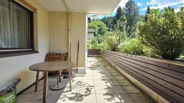 Geräumiger Balkon mit Fliesenboden, einem kleinen Tisch und Blick ins Grüne.