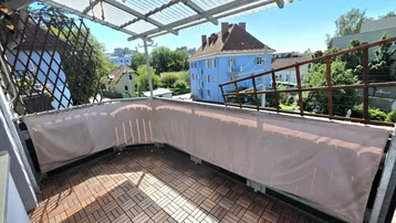Geräumiger Balkon mit Holzbodenfliesen und Überdachung, bietet einen Blick auf die Umgebung.
