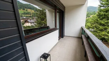 Balkon mit Holzbänken und schöner Aussicht auf die umliegende Berglandschaft und Häuser.