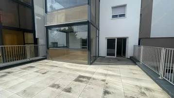Große geflieste Terrasse mit viel Platz und Zugang zu einem verglasten Bereich.