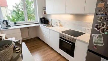 Moderne Küche mit weißen Schränken, Holzfußboden und Blick ins Grüne durch das Fenster.