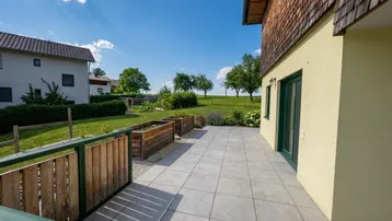 Große geflieste Terrasse mit Holzbeeten und weitem Blick ins Grüne, ideal für Entspannung im Freien.