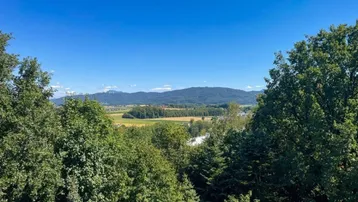 Weitläufiger Blick über grüne Felder und Wälder bis zu den fernen Bergen unter blauem Himmel.