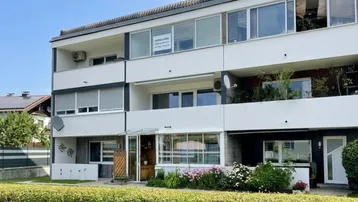 Mehrfamilienhaus mit mehreren Balkonen und gepflegter Gartenanlage im Vordergrund.