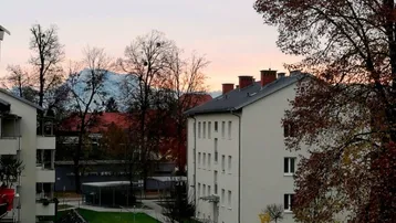 Abendlicher Blick auf Wohngebäude, Grünflächen und schneebedeckte Berge in der Ferne.