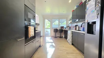 Moderne Küche mit dunklen Einbauschränken, integrierten Geräten und Zugang zum Balkon.