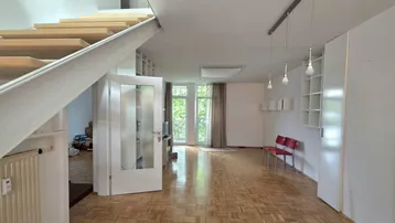 Helles Wohnzimmer mit Parkettboden, offener Treppe und großen Fenstern zum Außenbereich.