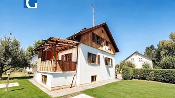 Einfamilienhaus mit Holzverkleidung im Dachgeschoss und einem gepflegten Gartenbereich unter blauem Himmel.