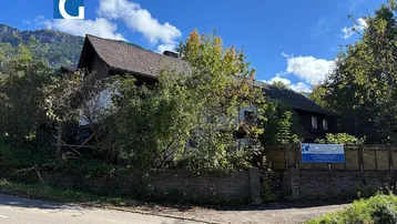 Traditionelles Haus mit Satteldach, umgeben von Bäumen und mit Blick auf die Berge.