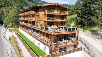 Modernes Holzgebäude mit mehreren Balkonen und Terrassen in alpiner Berglandschaft.