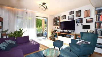 Helles Wohnzimmer mit lila Sofa, blauem Teppich und Zugang zum sonnigen Balkon.