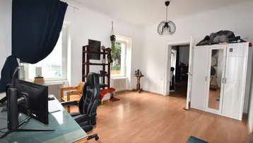 Geräumiges Zimmer mit Holzboden, großen Fenstern und einem Arbeitsbereich.