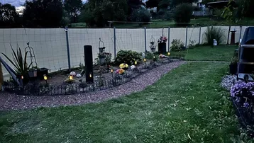 Gepflegter Gartenbereich mit dekorativer Beleuchtung und Kiesweg am Abend, umgeben von Grün.