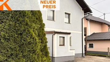 Seitenansicht eines Wohnhauses mit hellem Putz und einem großen Nadelbaum im Vordergrund.