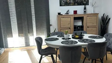 Lichtdurchfluteter Essbereich mit Holzboden, modernem Esstisch und vertikalen Fensterjalousien.