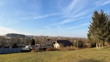 Weitläufige grüne Wiese mit Blick auf die umliegende Landschaft und entfernte Häuser unter blauem Himmel.