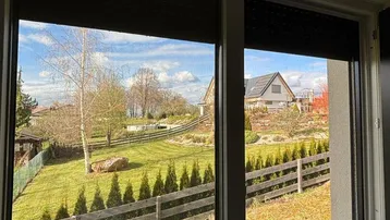Blick aus dem Fenster auf einen gepflegten Garten mit Zaun und umliegenden Häusern.