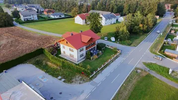 Luftaufnahme eines Einfamilienhauses mit rotem Dach, umgeben von Grünflächen und einer Straße.