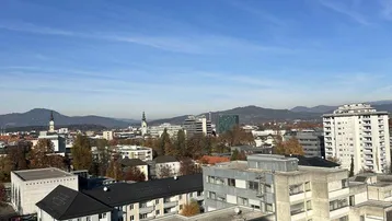 Weitläufiger Blick über die Stadt mit Bergen im Hintergrund unter blauem Himmel.