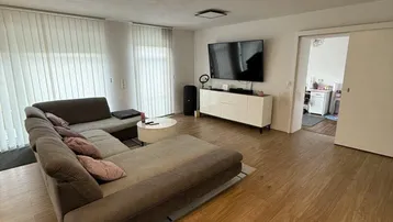 Geräumiges Wohnzimmer mit großem Ecksofa, Holzboden und Blick in die Küche.