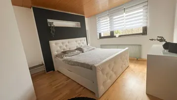 Gemütliches Schlafzimmer mit Holzbalkendecke, großem Bett und Fenster mit Blick ins Grüne.
