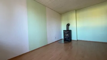 Gemütliches Wohnzimmer mit Holzboden, Kaminofen und hellgrünen Akzentwänden.