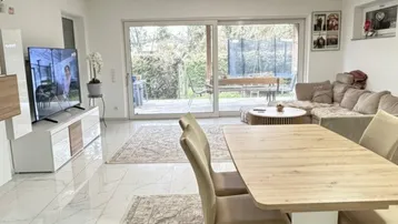 Heller Wohn- und Essbereich mit modernen Fliesen, großem Esstisch und Zugang zur Terrasse.