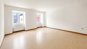 Helles, leeres Zimmer mit Laminatboden und zwei Fenstern, bereit zur individuellen Gestaltung.