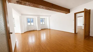 Geräumiges Wohnzimmer mit hellem Parkettboden und einem dekorativen Holzbalken an der Decke.