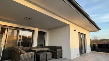 Geräumige Terrasse mit modernen Outdoor-Möbeln und Fliesenboden unter blauem Himmel.