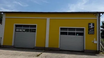 Gelbes Gebäude mit zwei Garagentoren und einem großen Betonvorplatz unter blauem Himmel.