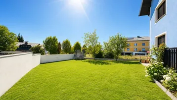 Großer, gepflegter Rasenbereich mit Trampolin und sonniger Ausrichtung neben dem blauen Haus.
