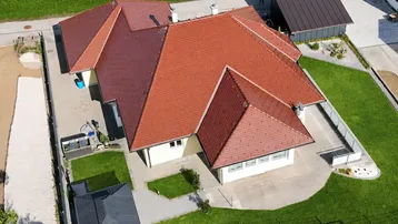Luftaufnahme eines Hauses mit rotem Ziegeldach, gelber Fassade und gepflegtem Garten.