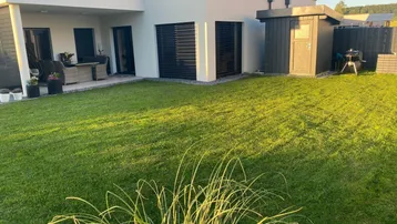 Modernes Haus mit großem, gepflegtem Rasen, einer möblierten Terrasse und einem Gartenschuppen.