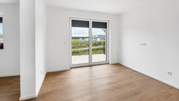 Lichtdurchfluteter Raum mit Laminatboden und Zugang zu einem französischen Balkon.